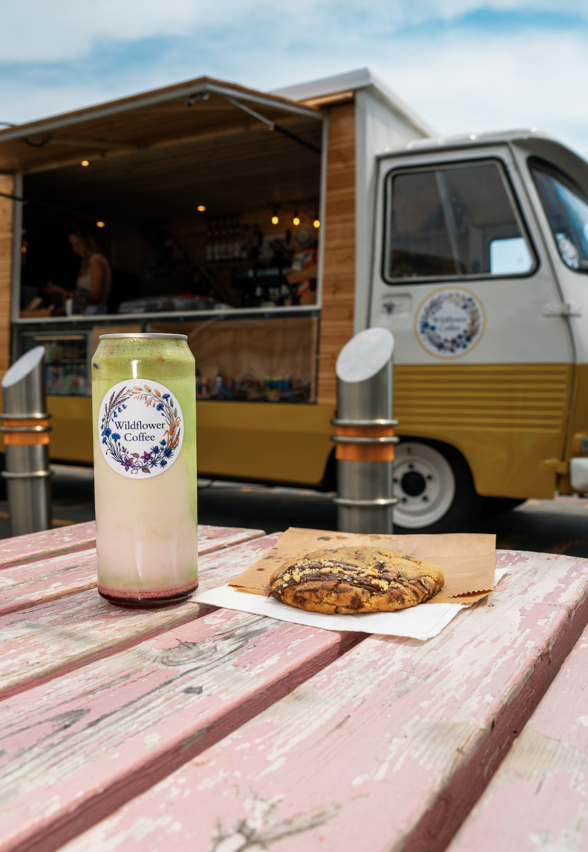 An iced matcha and a stuffed cookie on a picnic table in front of the van